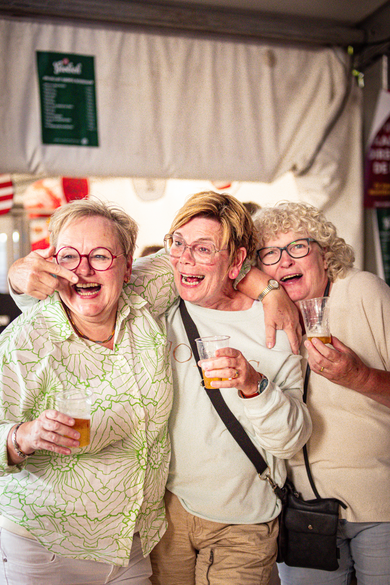 Three older women standing in front of a tent with one woman playfully making a silly face.