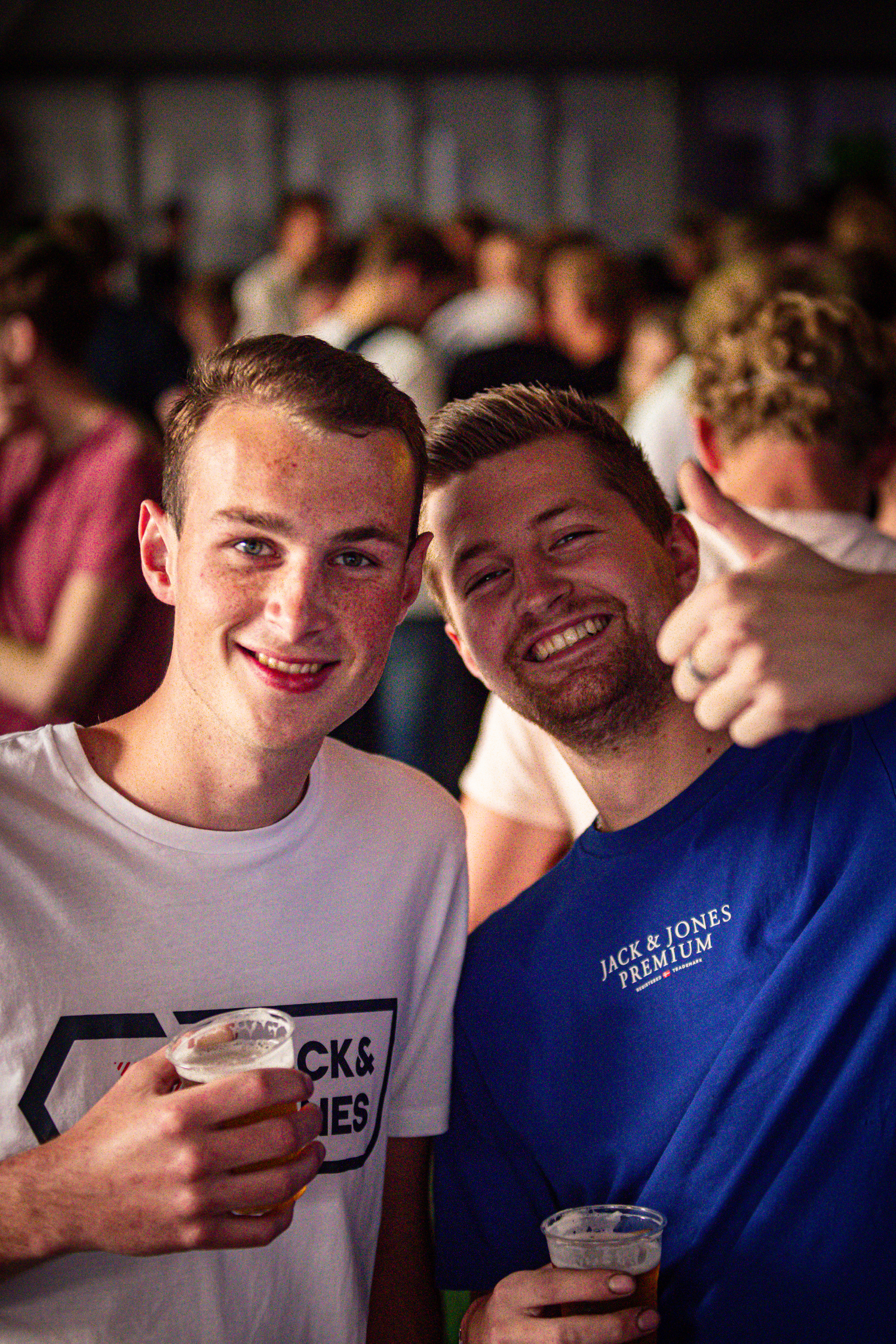 Two young men pose for a picture at Kermis Boerhaar, enjoying drinks and the festive atmosphere.