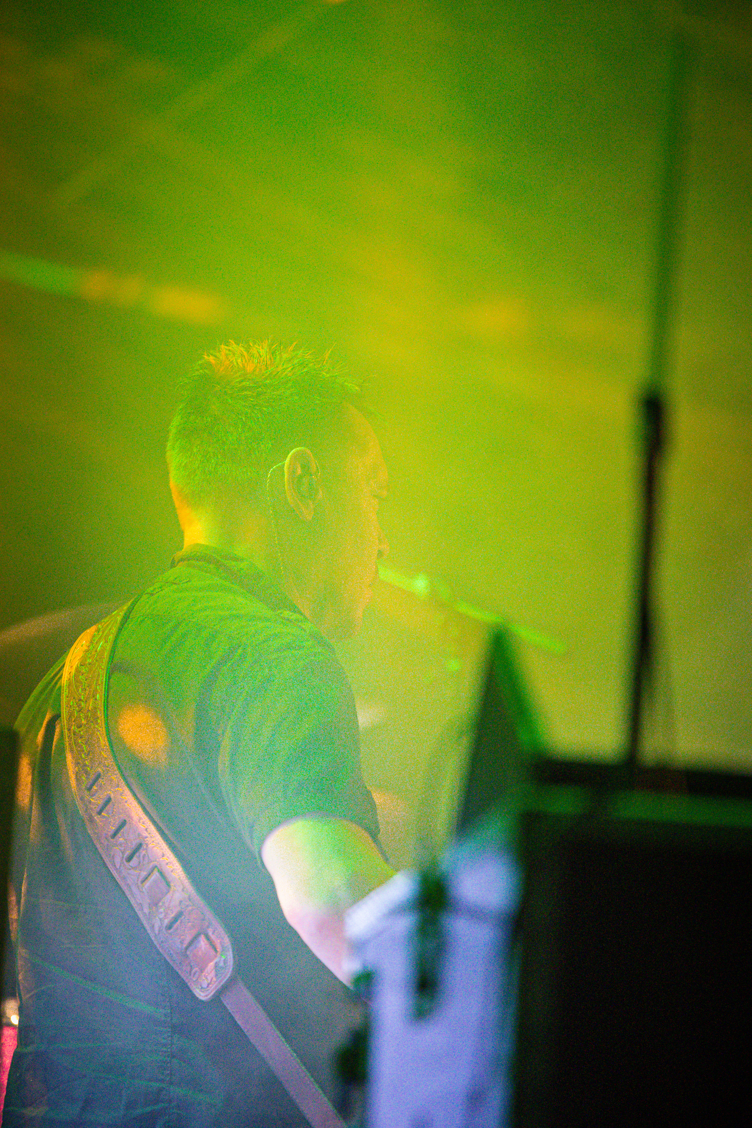 A man plays an electric guitar with a neon green background.