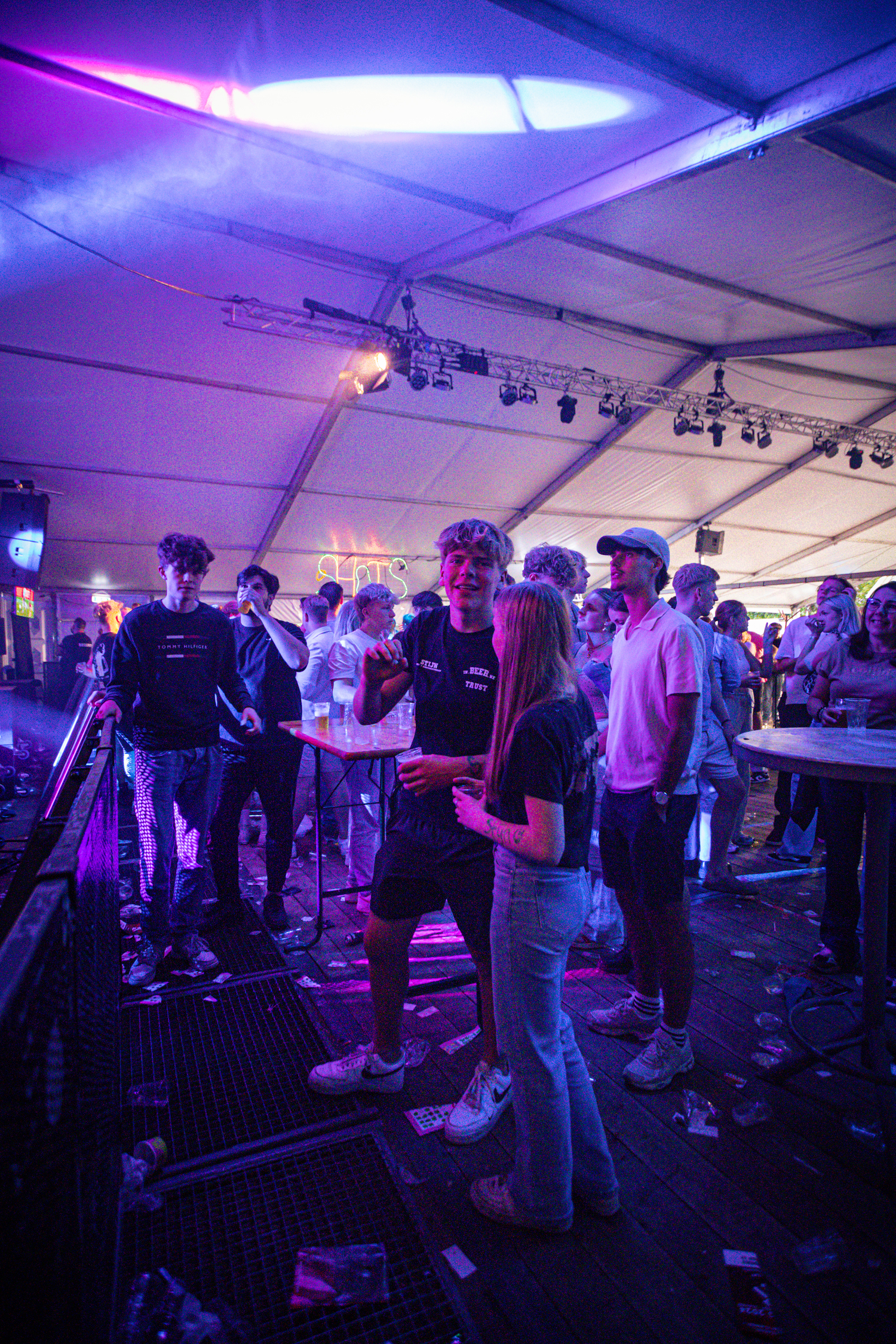 A large group of people standing and talking in a venue with bright purple lights.