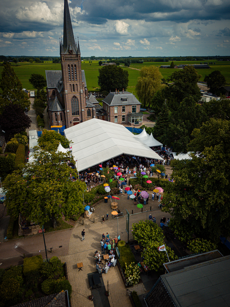 Een openluchttheater op een kermis waar volk en kinderen bijeen zijn.