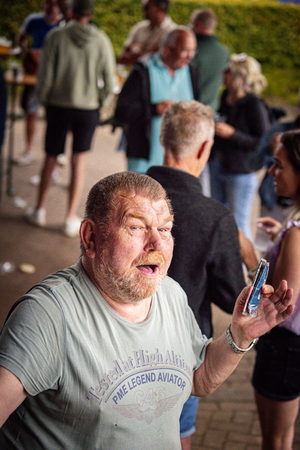 A man showing his phone to a crowd of people at an outdoor event, with a sign behind him that says "Middag & avond".