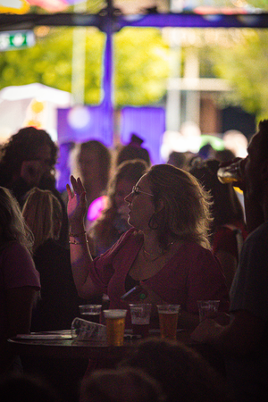 A group of people in a bar, one is wearing a red shirt and another has a beer.