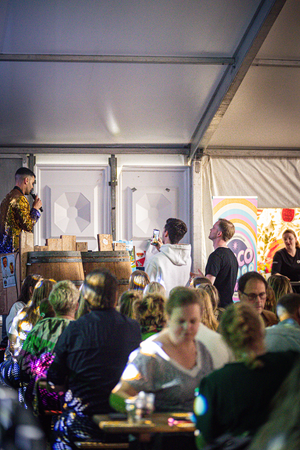 A group of people are sitting at tables in a tent, enjoying the Kermis Boerhaar. The atmosphere is lively and festive.