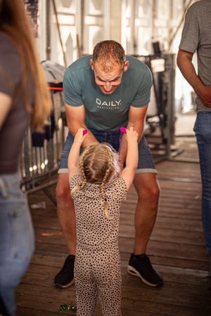 A man in a blue shirt helps a little girl with her hands.