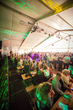 A festive scene with a crowd of people gathered around food tables and standing in a line.