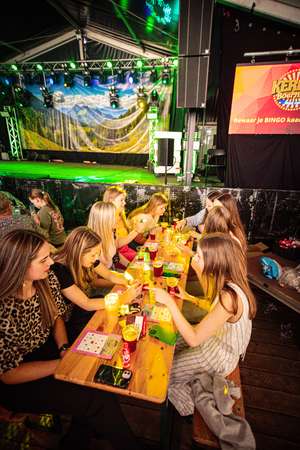 A group of people at a table in a dark room with a Kermis Boerhaar sign on the wall.