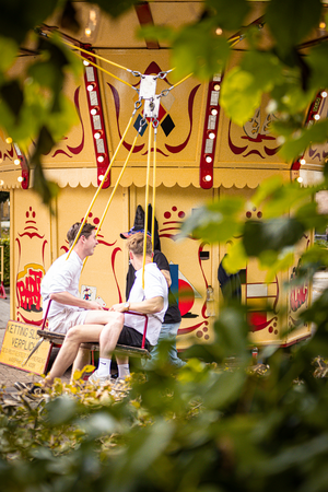 Two men sitting at a bar in a carnival, one of them is wearing sunglasses.