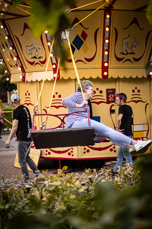 A woman wearing a striped shirt and jeans is sitting in a hanging basket at Kermis Boerhaar.