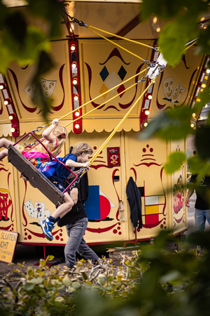 A woman is lifting a child into an amusement park ride at the Kermis Boerhaar.