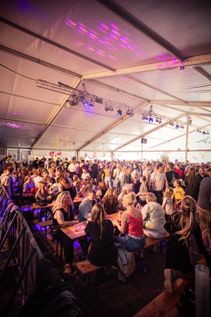 A large group of people are gathered in a white tent with colorful lights at Kermis Boerhaar.