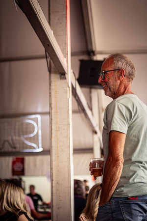 A man stands in a room at the Kermis Boerhaar, holding his beer.