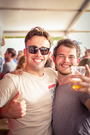 Two men in sunglasses pose for a photo, one holding a beer.