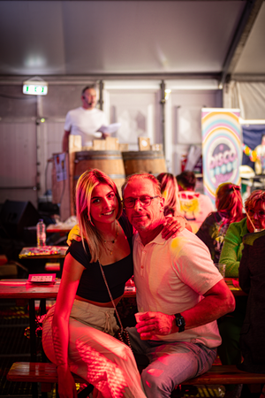 Two people posing for a photo at Kermis Boerhaar with a rainbow flag in the background.