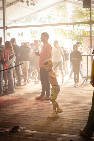 A group of people are standing around a stage at Kermis Boerhaar, the event is held during daytime.