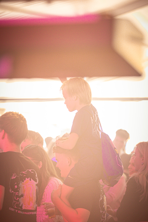 a person standing on a bar in front of a crowd, with a child sitting on their shoulders.