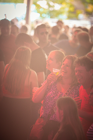 A group of people are at a festival with a red tent in the background.