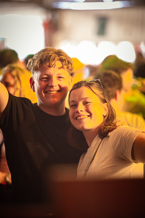 Two people taking a selfie on the street in front of a crowd.