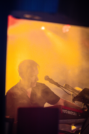 A man playing a red electric guitar with fog in the background.