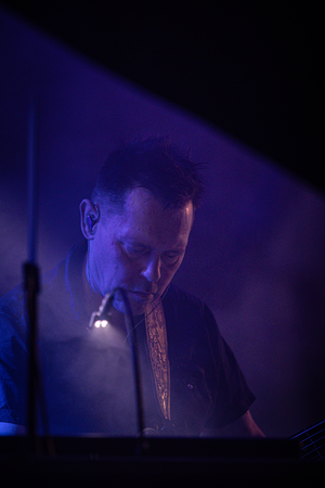 A man with a microphone in his hand, wearing a black shirt and blue pants is singing on stage.