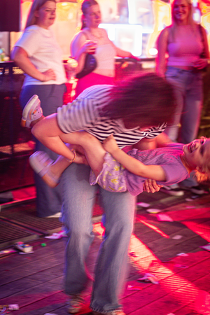 A woman in jeans lifts a child wearing a purple shirt.