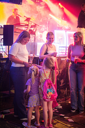 A woman in a pink shirt and blue jeans wearing glasses holding a small child's hand.