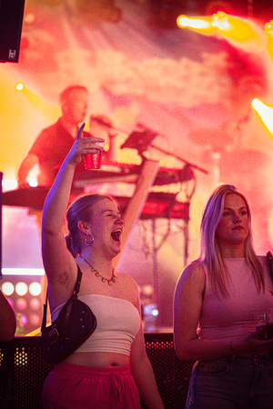 Two girls are at a concert with their arms raised.