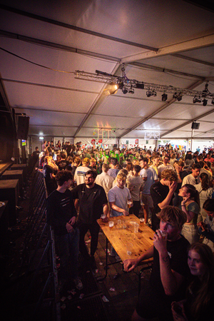 A large crowd of people gathered around a bar in a tent.