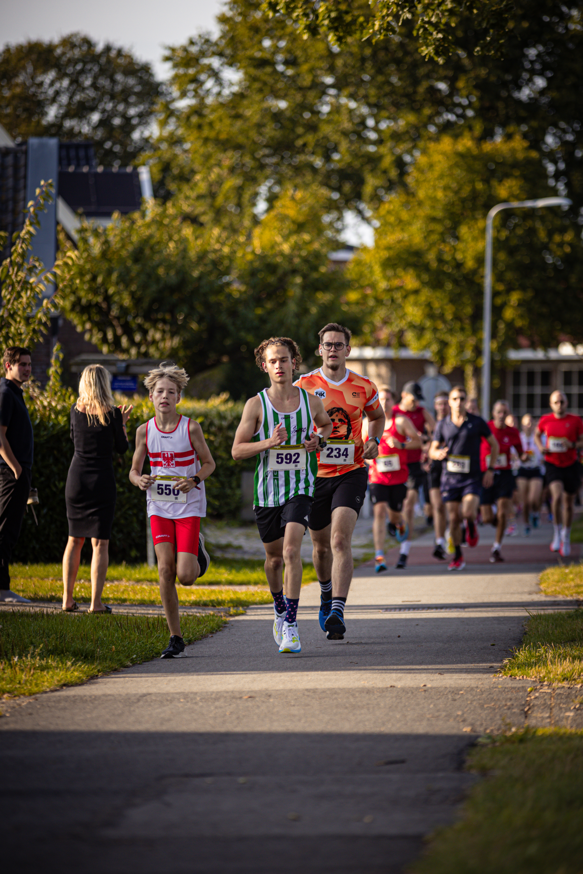 A group of runners wearing bibs with numbers like 261, 262, and 263 race down a city street.