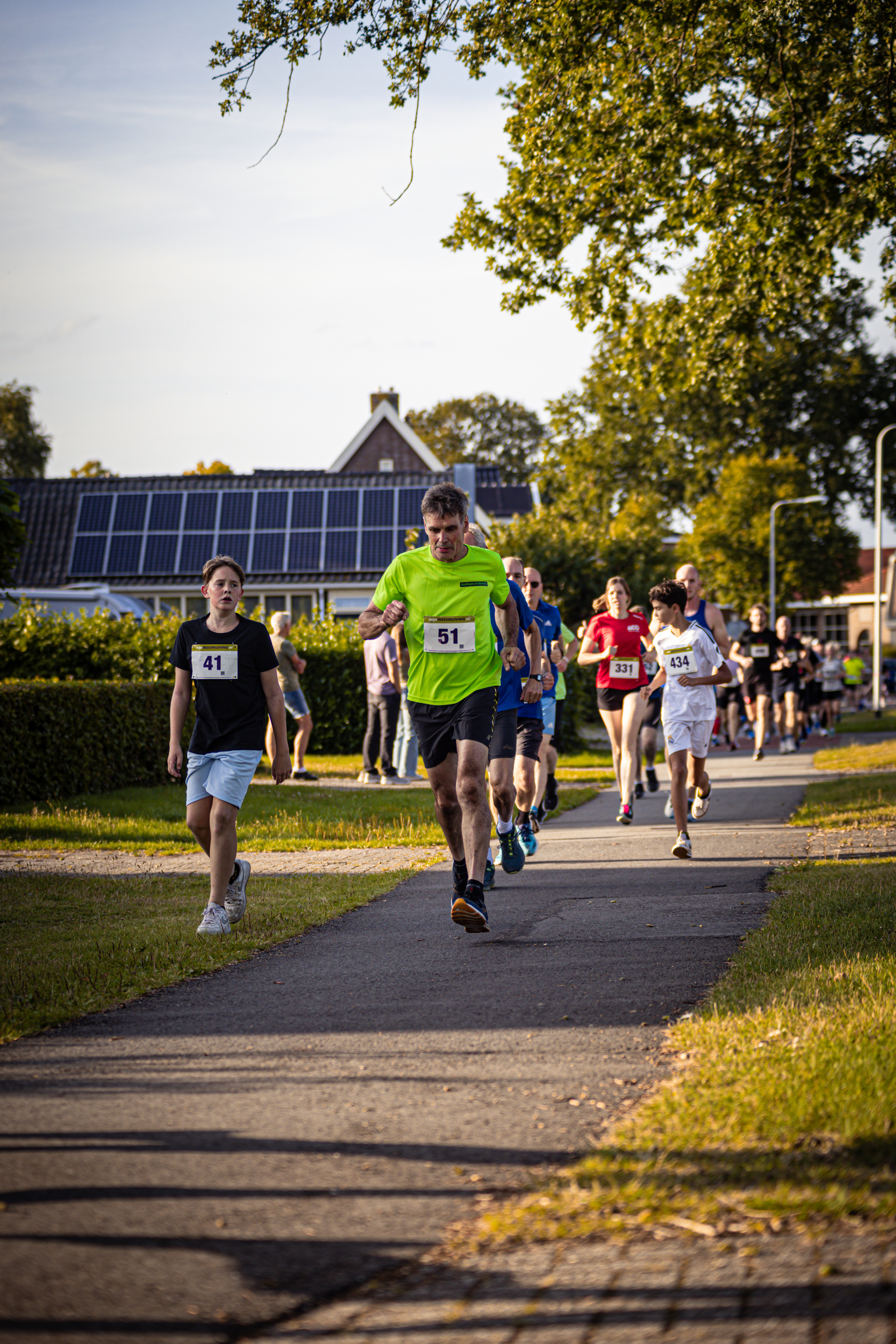 A group of people participating in a running race, with numbers on their backs and wearing athletic shoes.