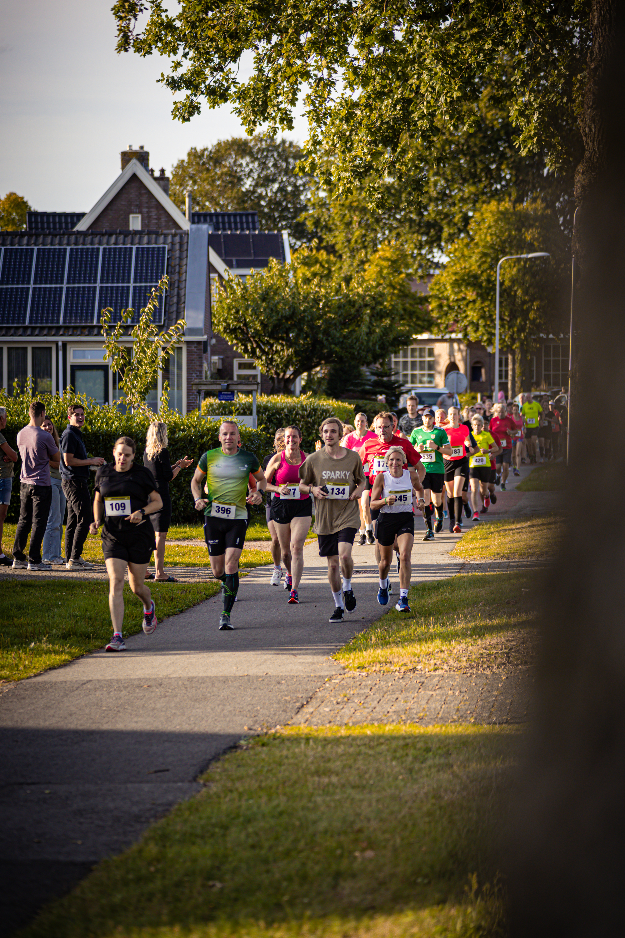 People participating in a marathon on the streets of the town, with houses and trees in the background.