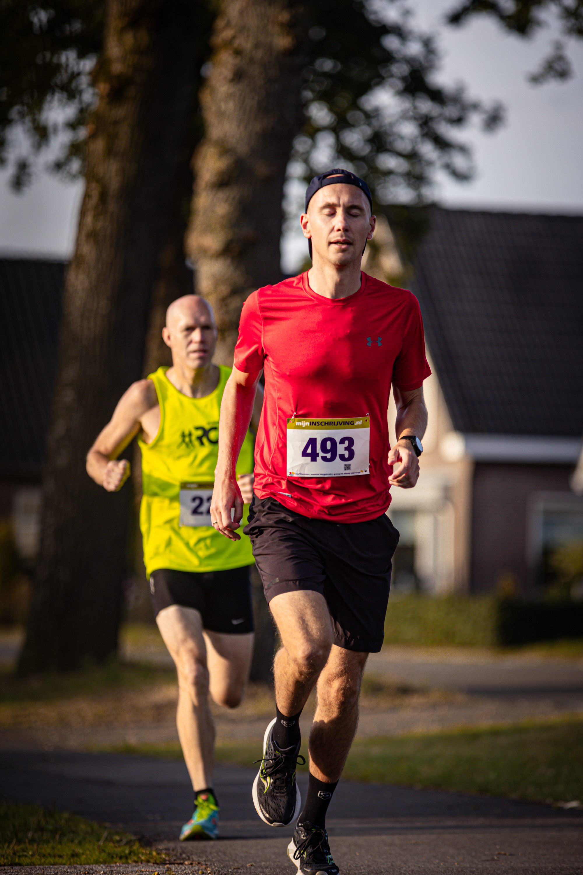 Two runners are running on the road. The runner in front is wearing a red shirt with the number 433 on it.