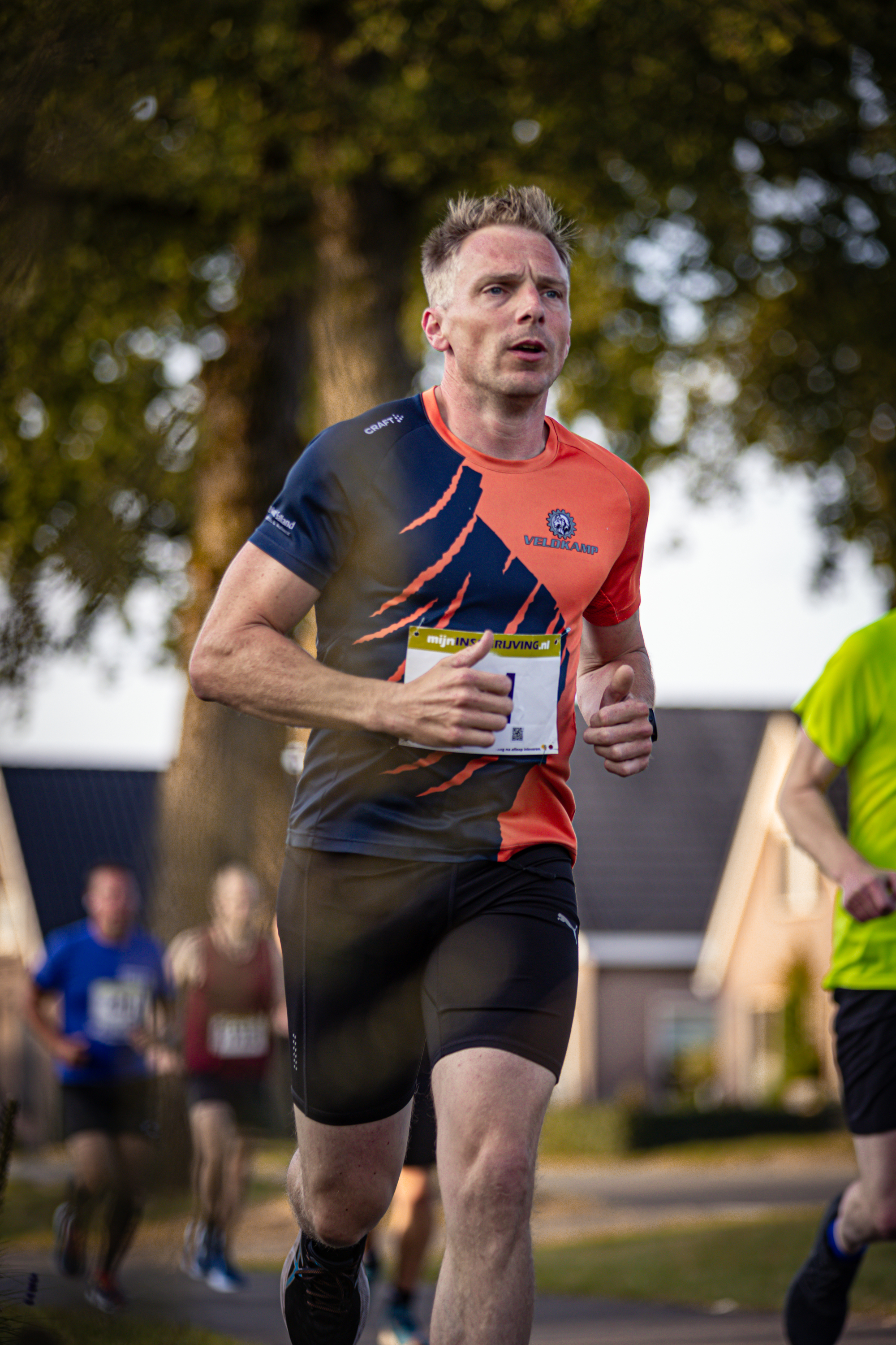 A man running in a marathon with an orange and black shirt on.