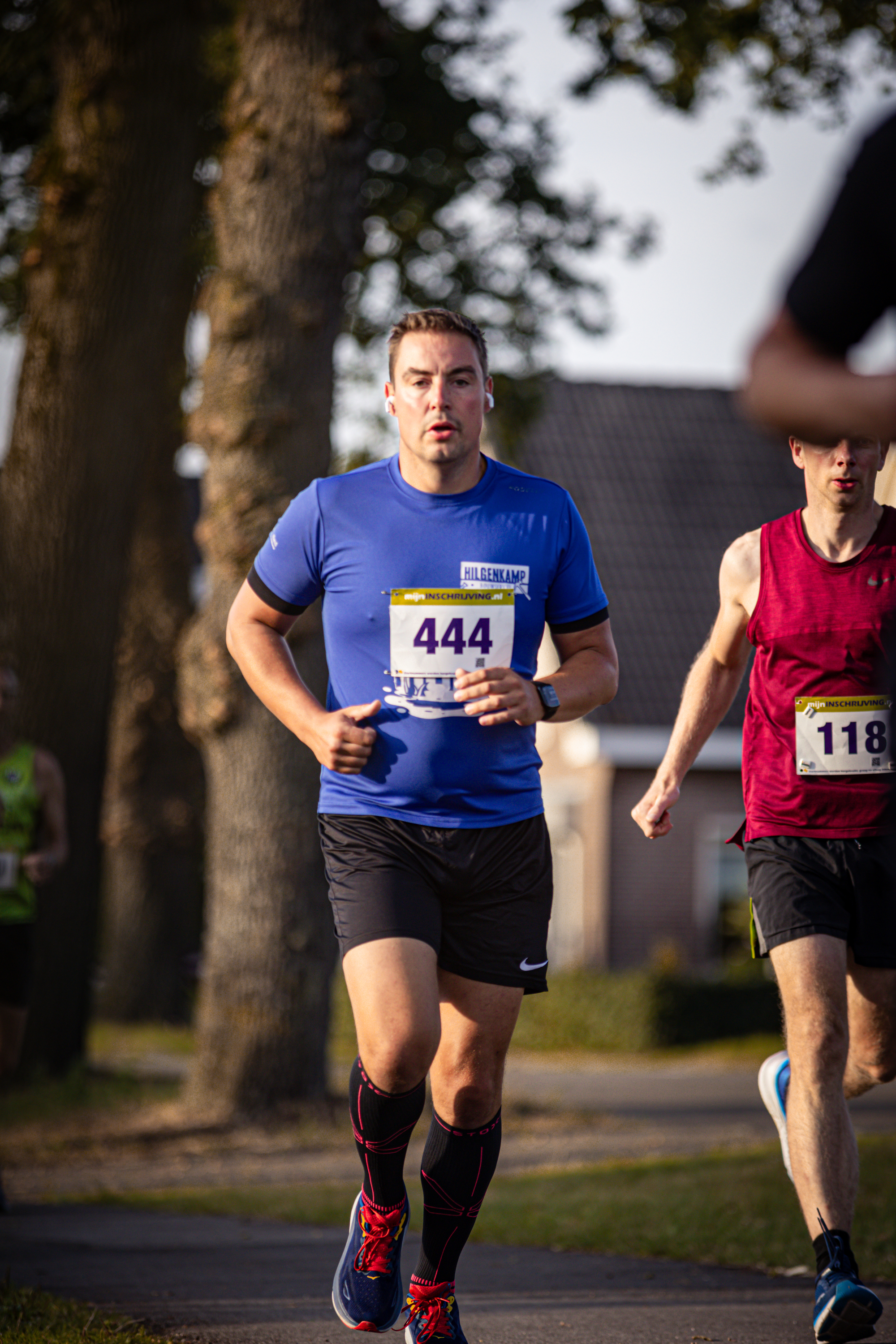 Two runners on a path with numbers 444 and 118 in hand.