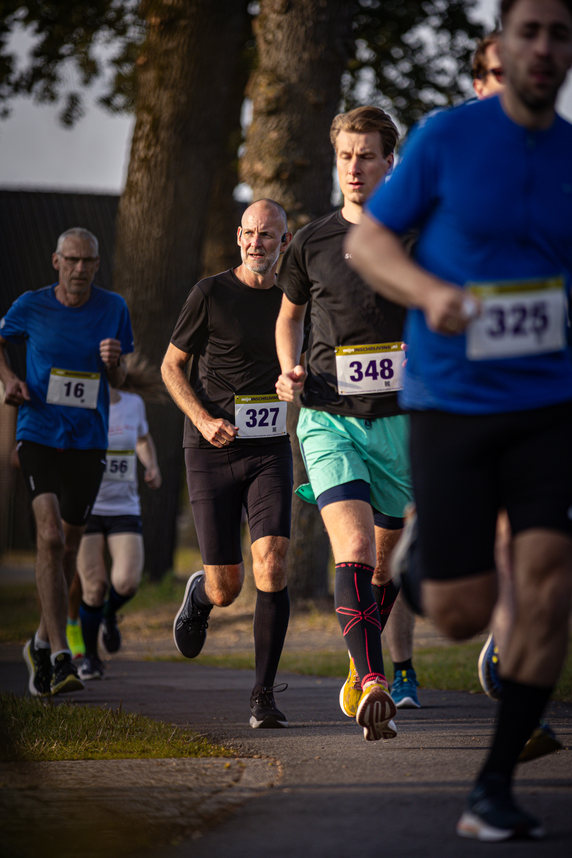 A race taking place with 3 runners. One runner is wearing the number 348 and another is wearing 327.