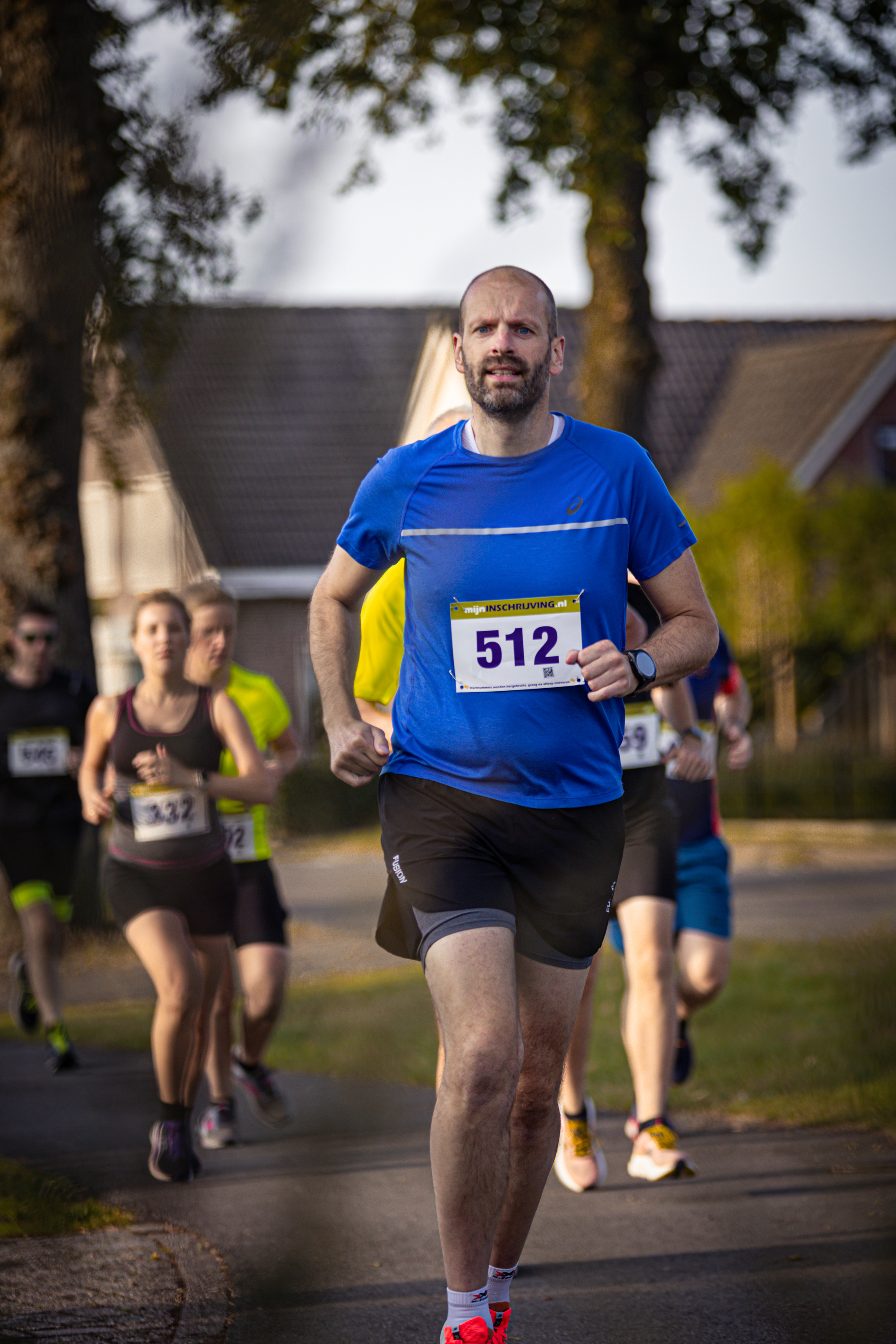 A man wearing a blue shirt with the number 512 on it runs next to a group of people.