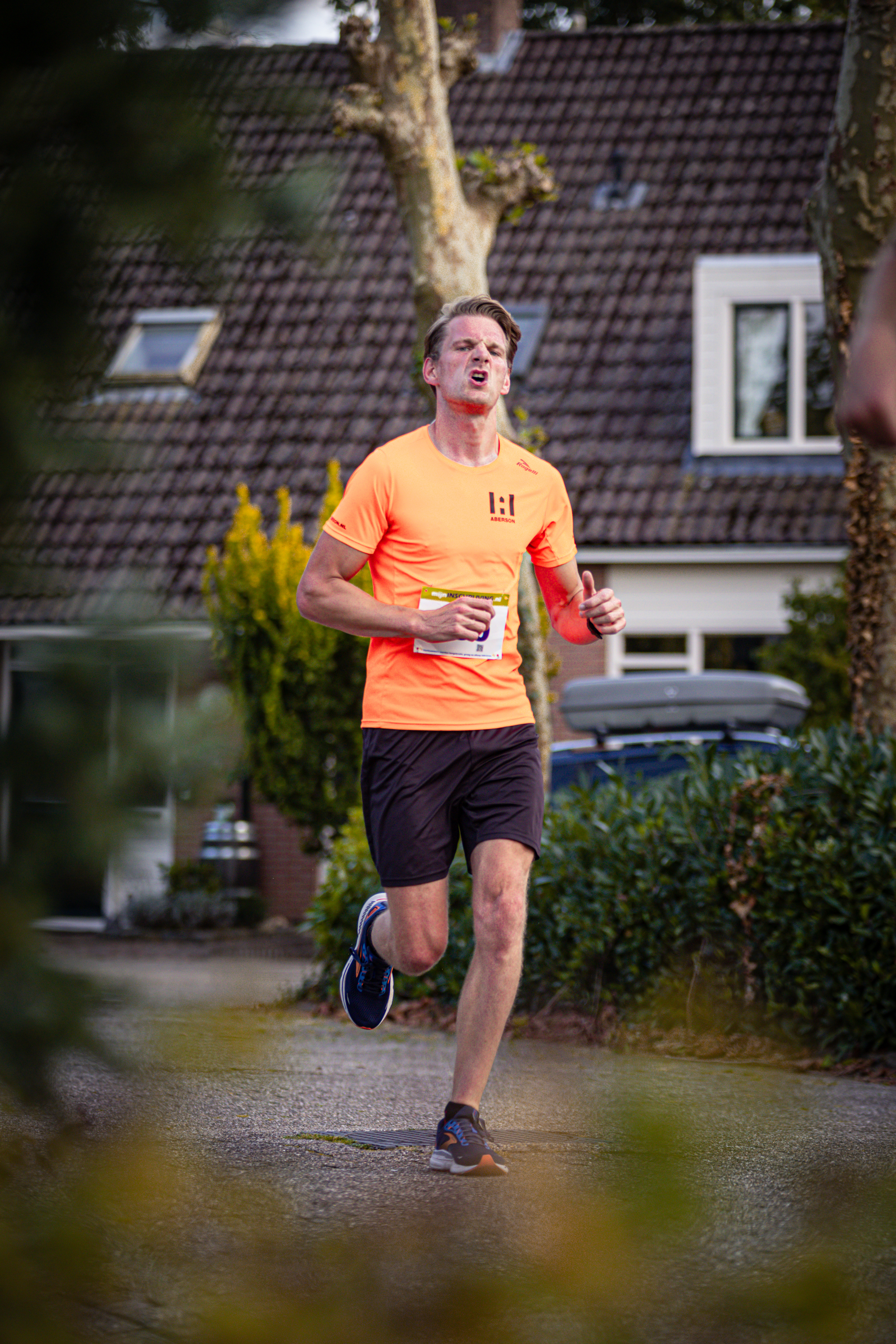 A man runs down a street with an orange shirt and black shorts.