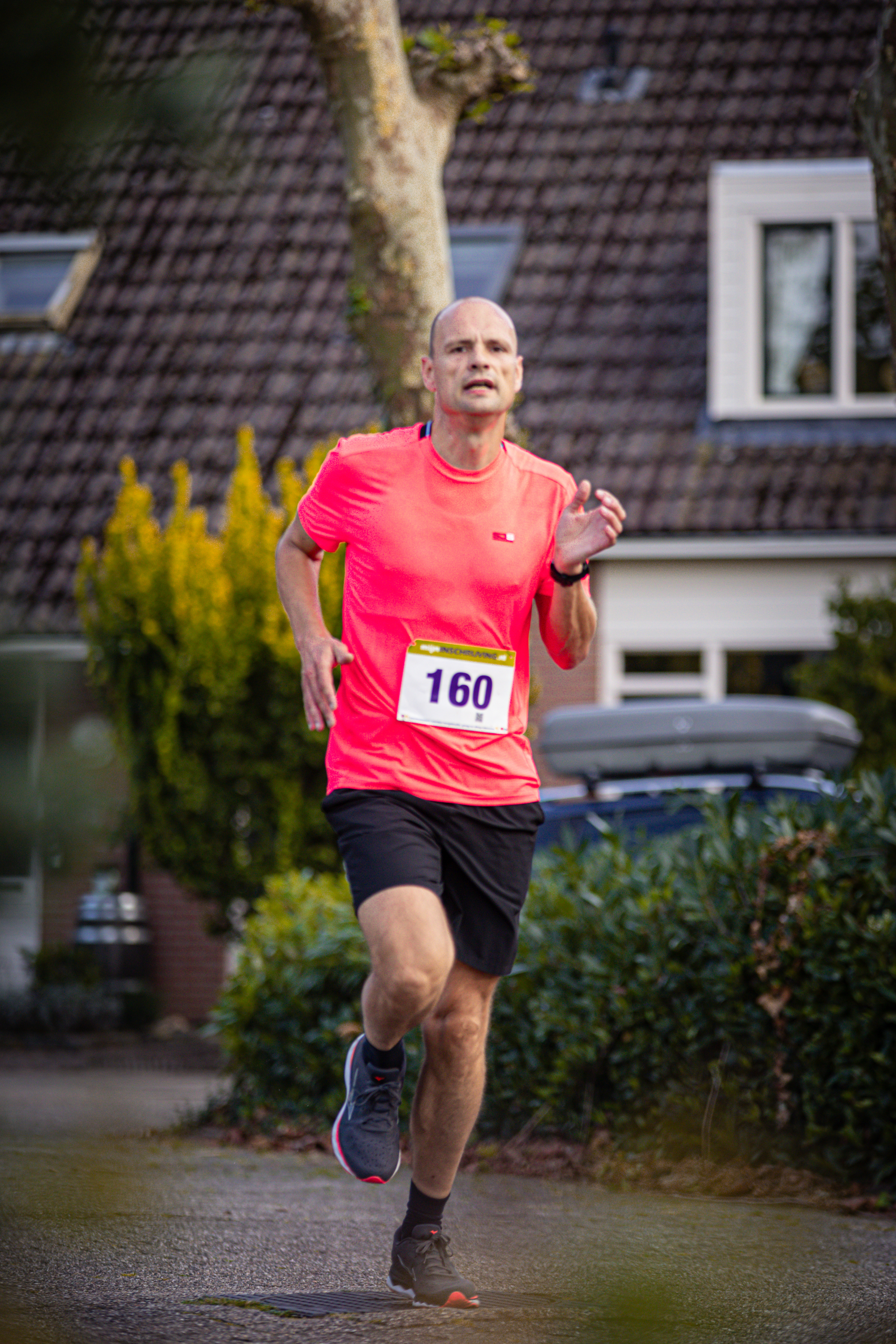 A bald man running with a pink shirt that has number 160 on it.