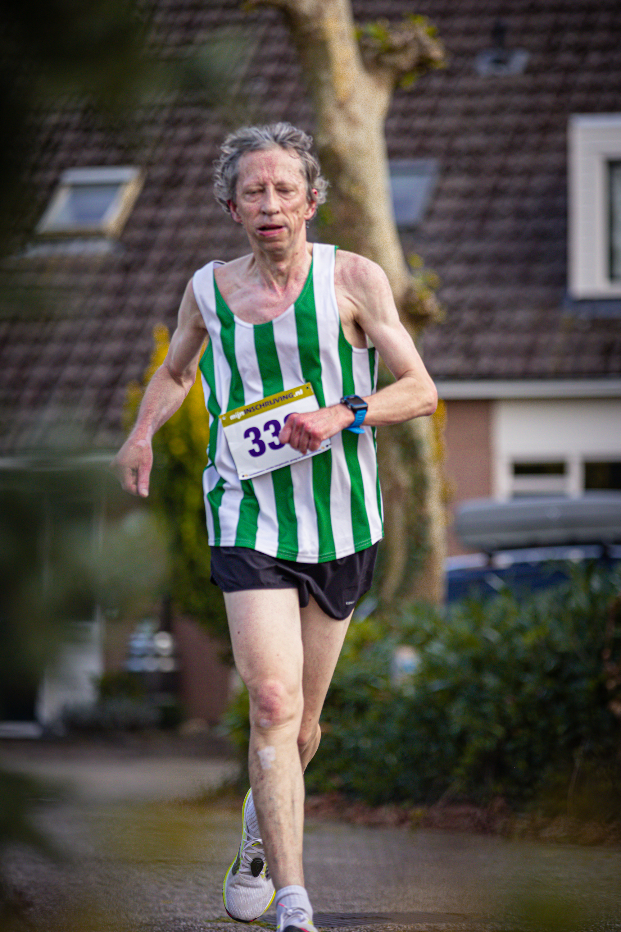 A man wearing a green and white striped tank top with the number 32 on it. He is running outside.