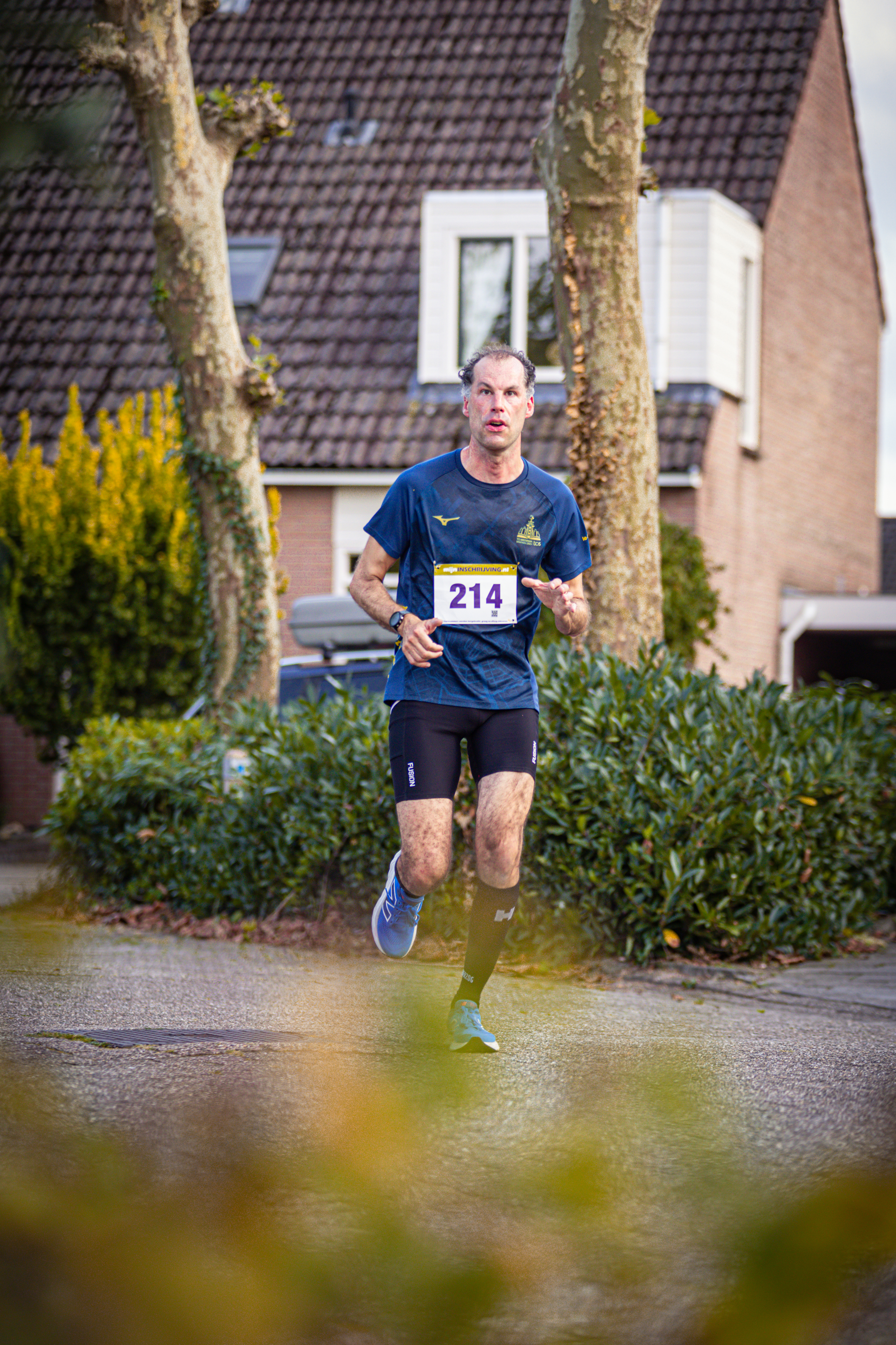 A runner in a blue shirt with the number 214 runs down a street.