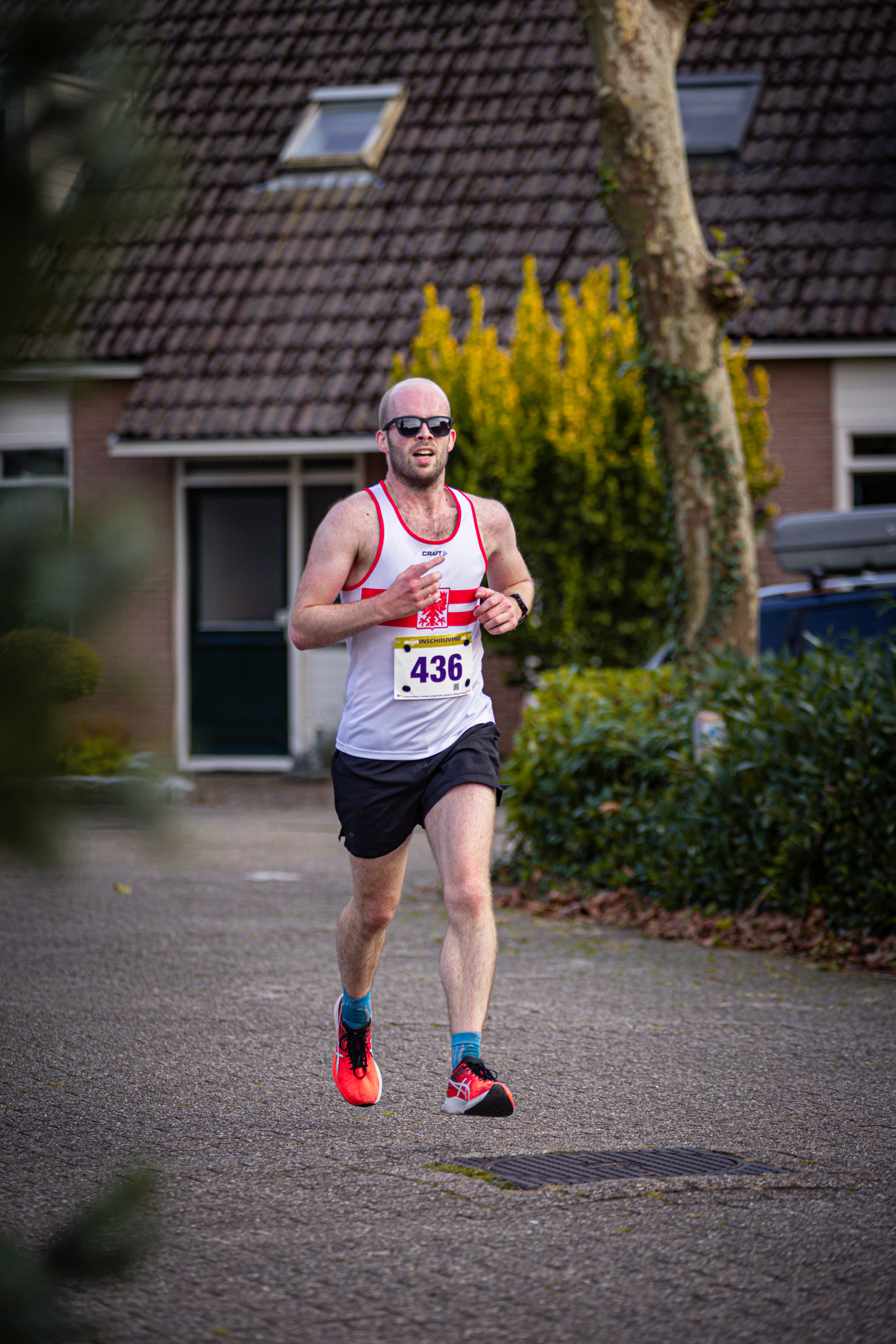 A man is running in a street with 4:49 on his shirt and red sunglasses on his face.