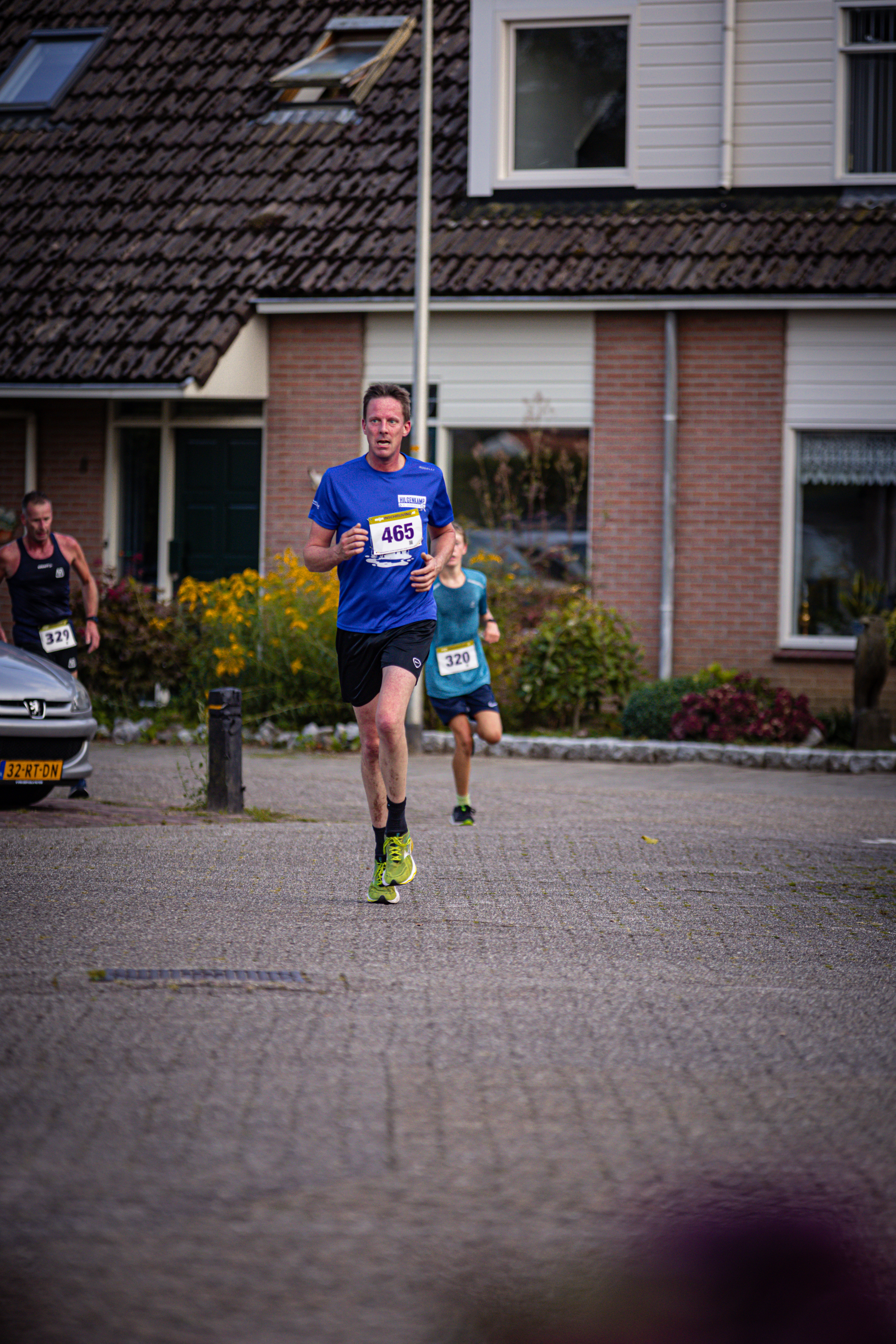 A man is running on a street and has the number 3 on his shirt. He is wearing blue shorts and blue shoes.