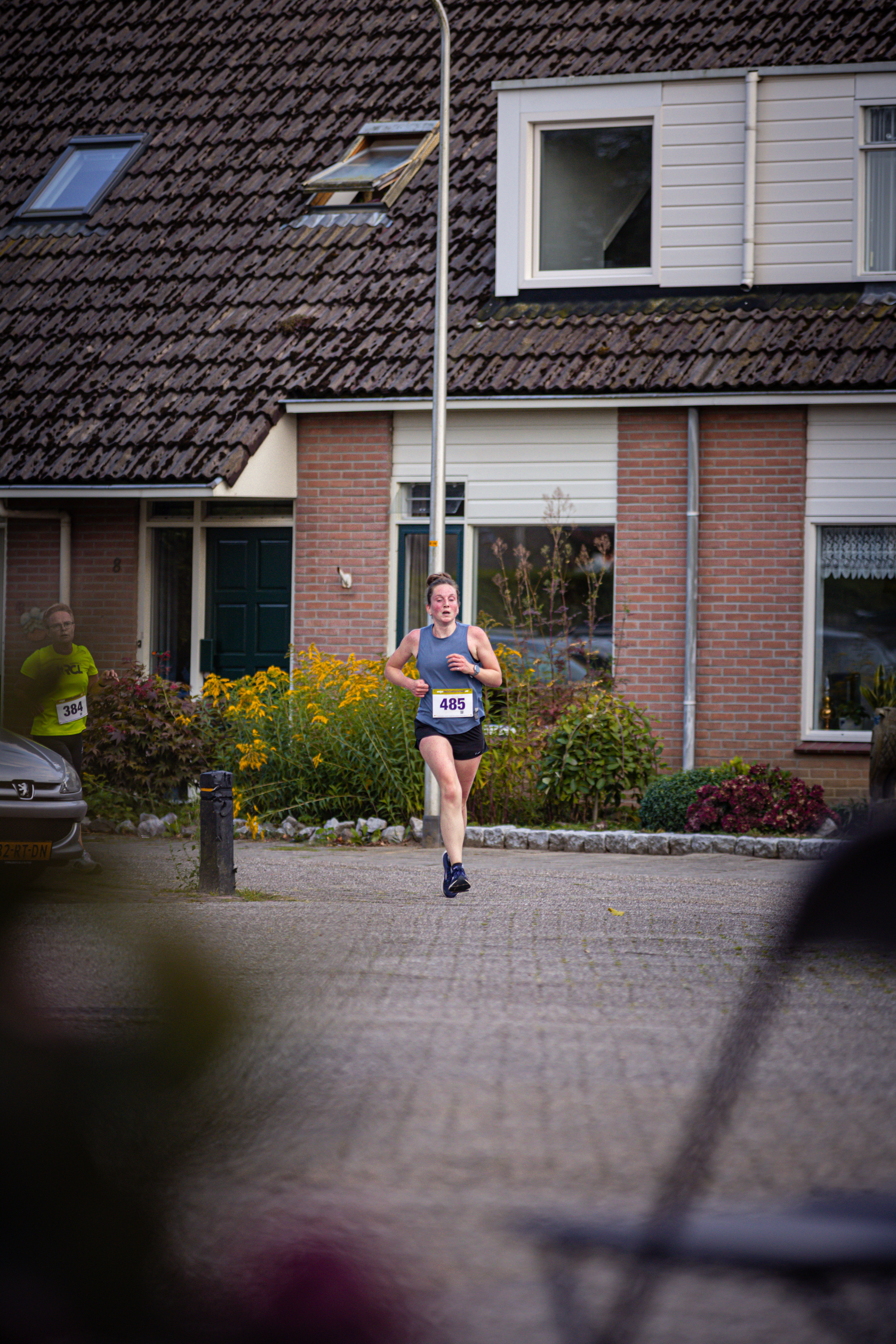 A woman in a blue tank top and black shorts runs down the street.