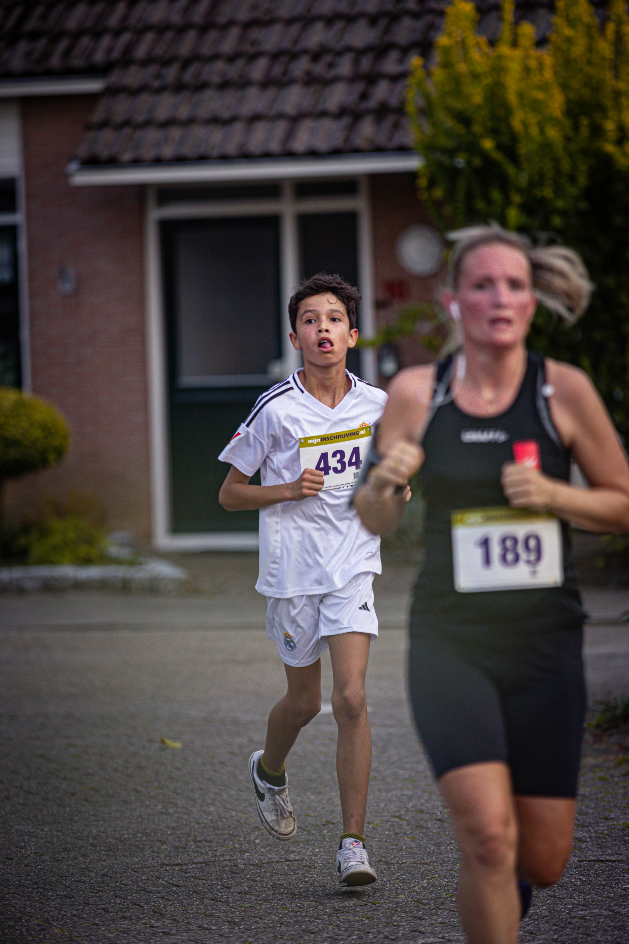 A girl running behind a boy wearing number 394. They are both participating in a race sponsored by Adidas and Nike.