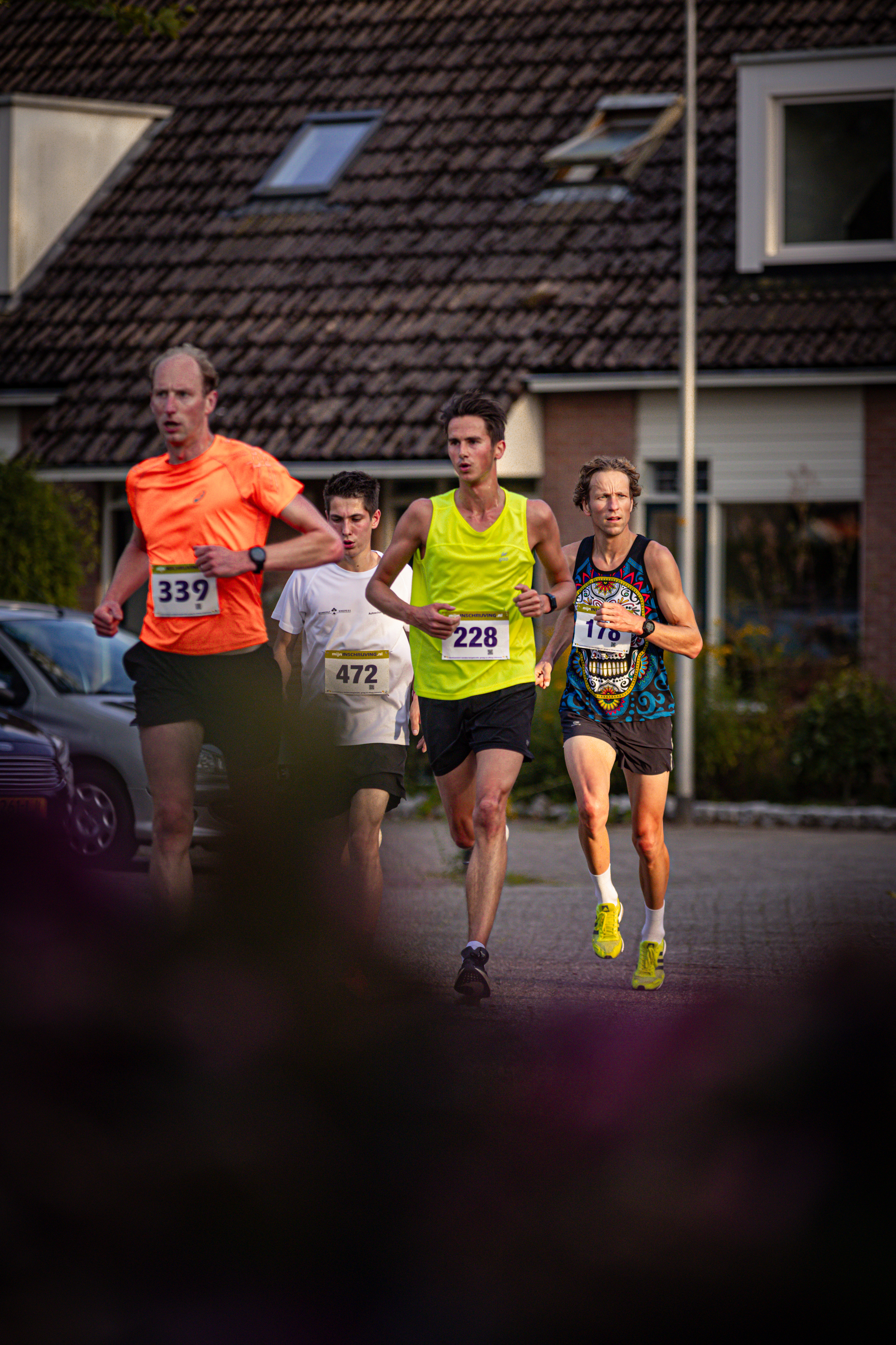 Three men running on a road with one wearing a shirt that says Pomploop.