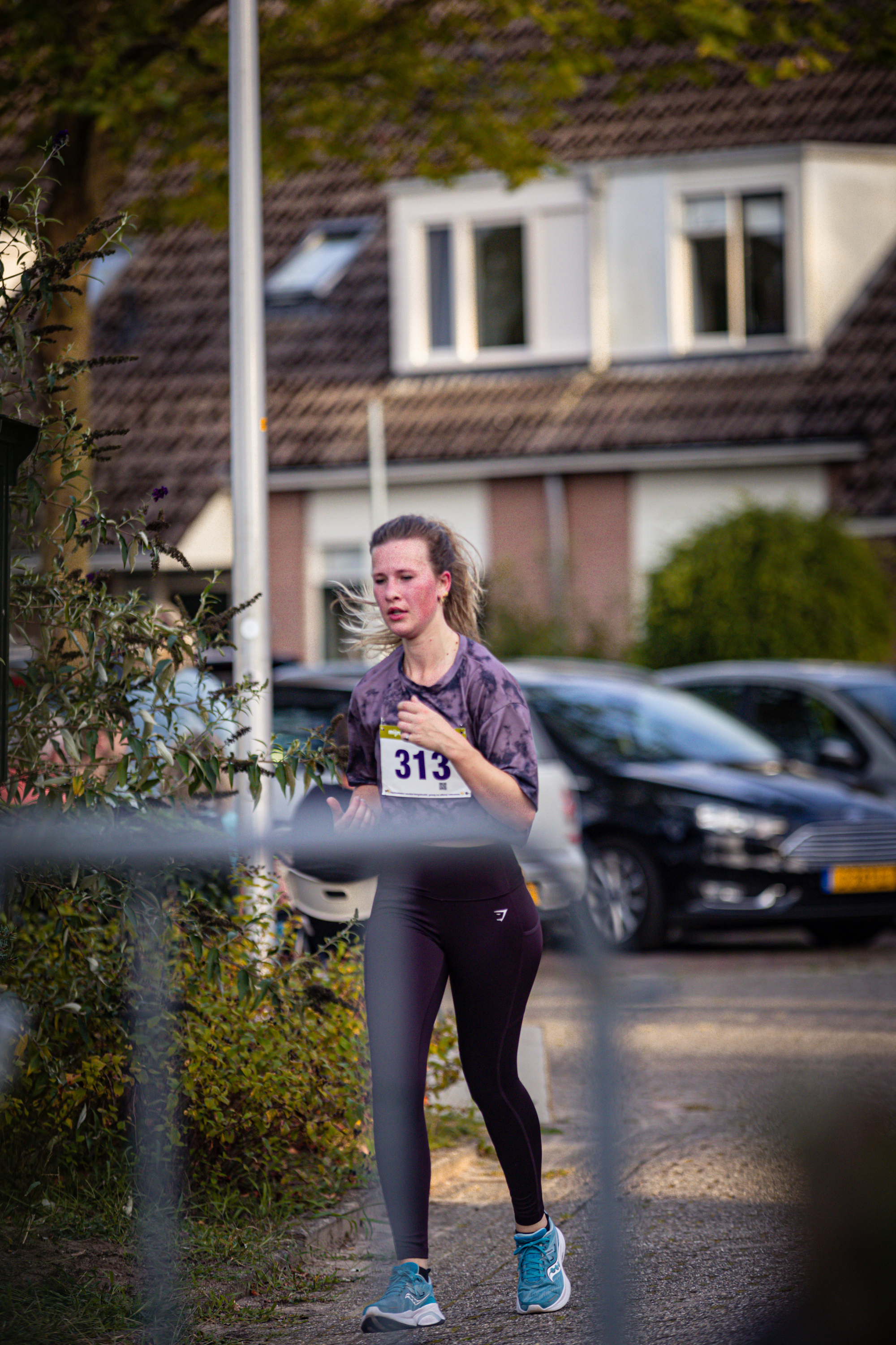 A woman runs on the road while wearing a black tank top and blue and white sneakers.