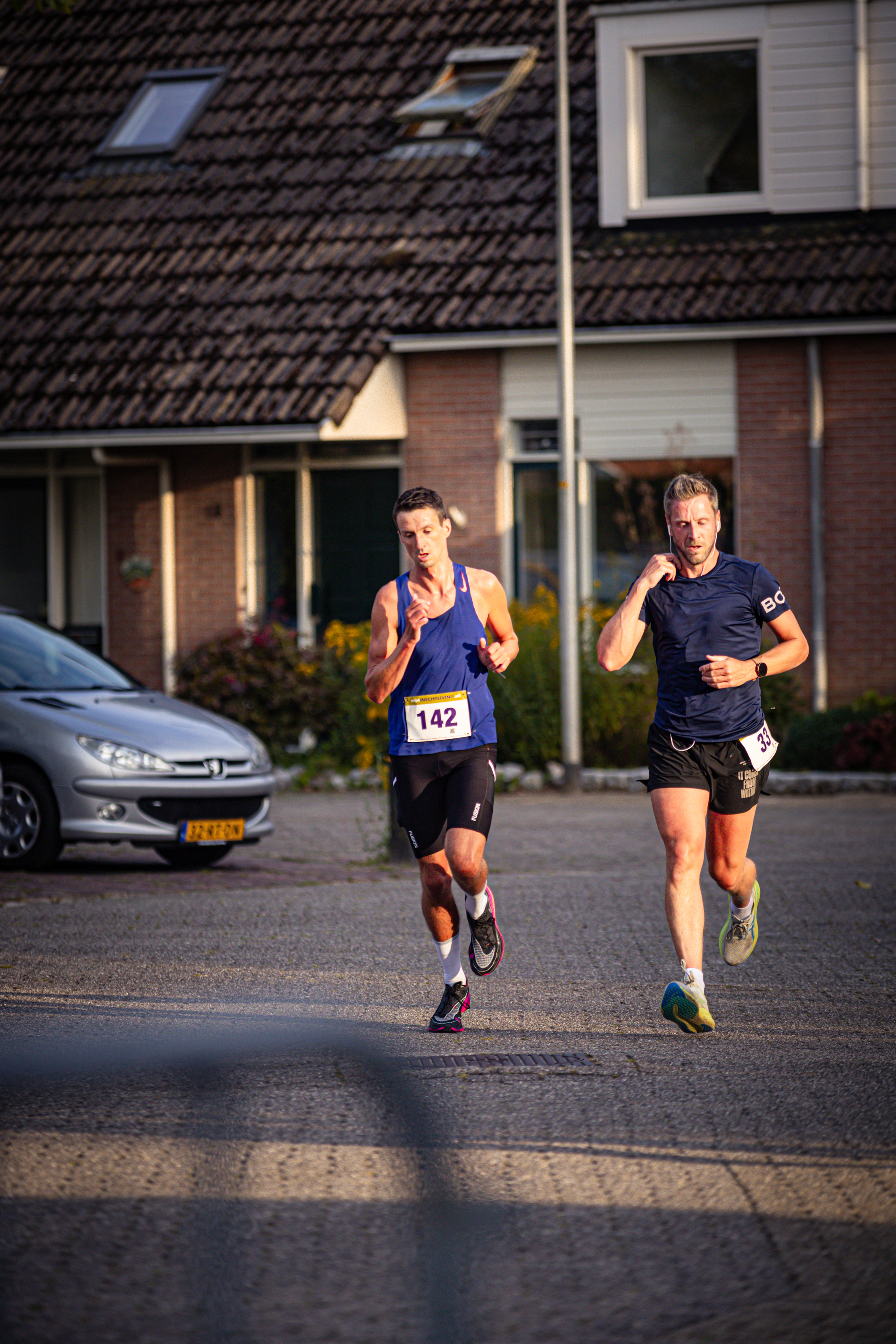 A couple of people run through a town with one wearing the number 15 on their shirt.