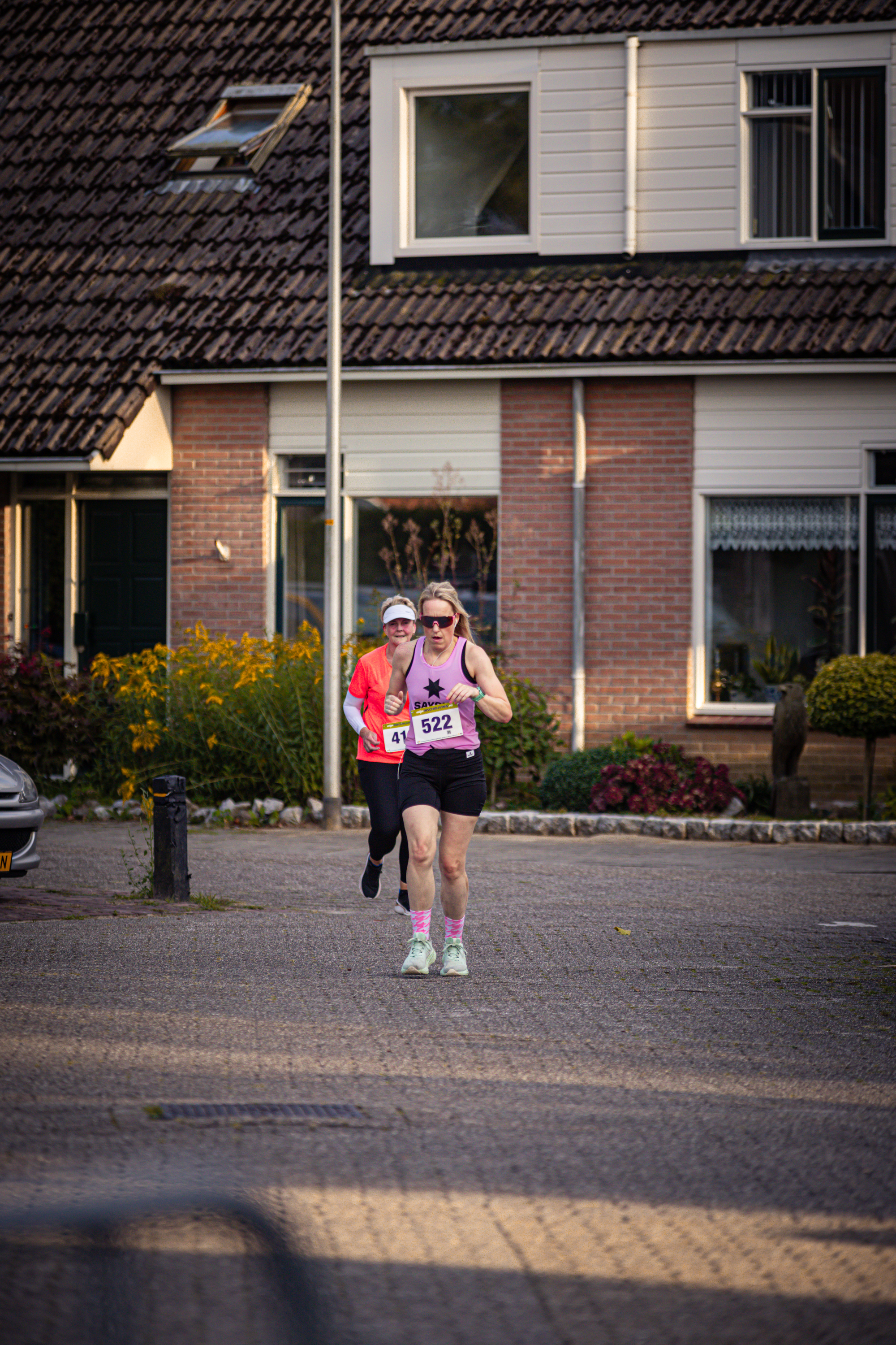 Two women running with one wearing a pink tank top that says "POMPLOP" on it. They are wearing pink and black sneakers.