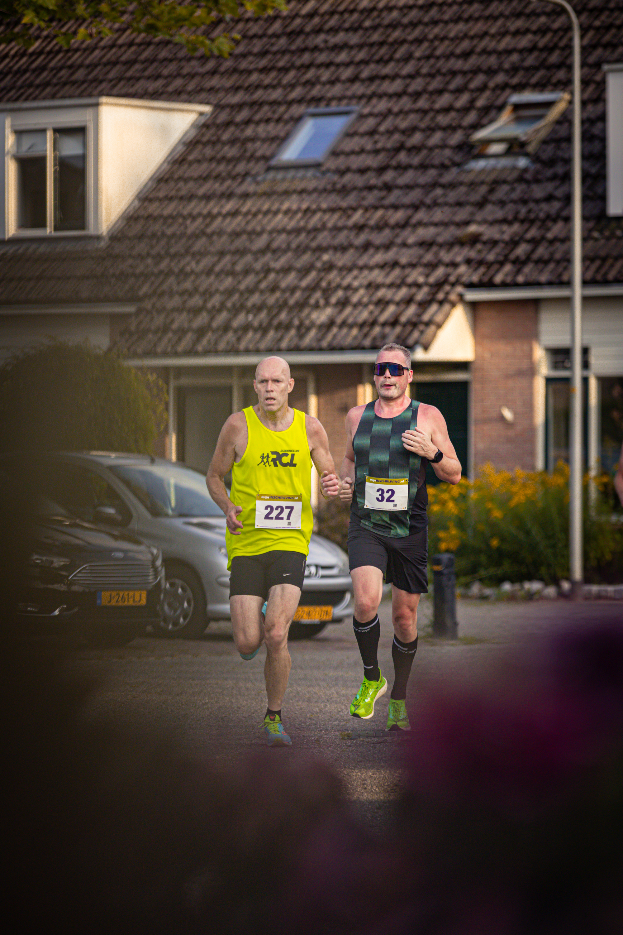 Two runners on a street with one wearing a black tank top and the other a yellow shirt.