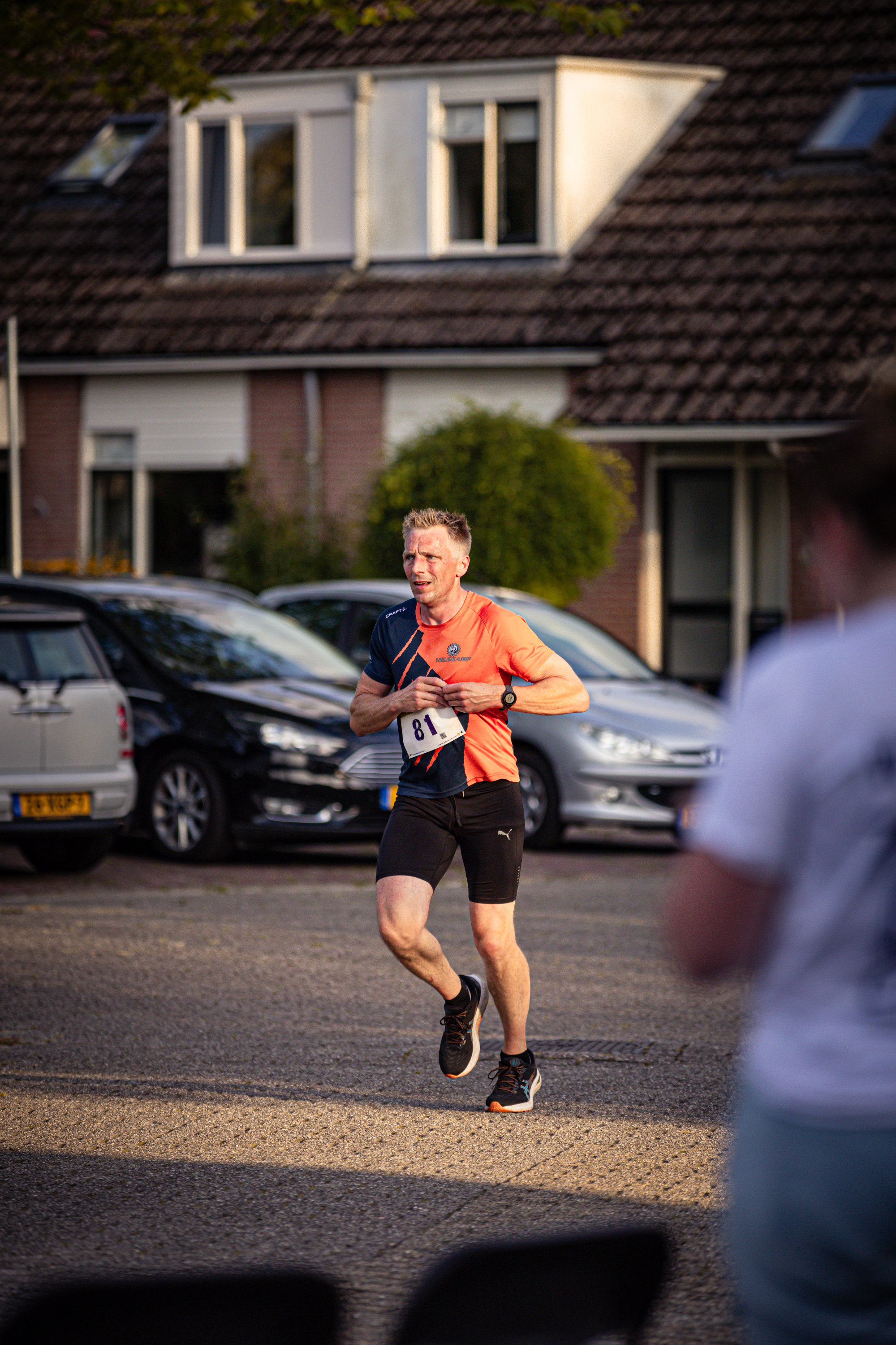 A man running with a red shirt on in front of two cars.